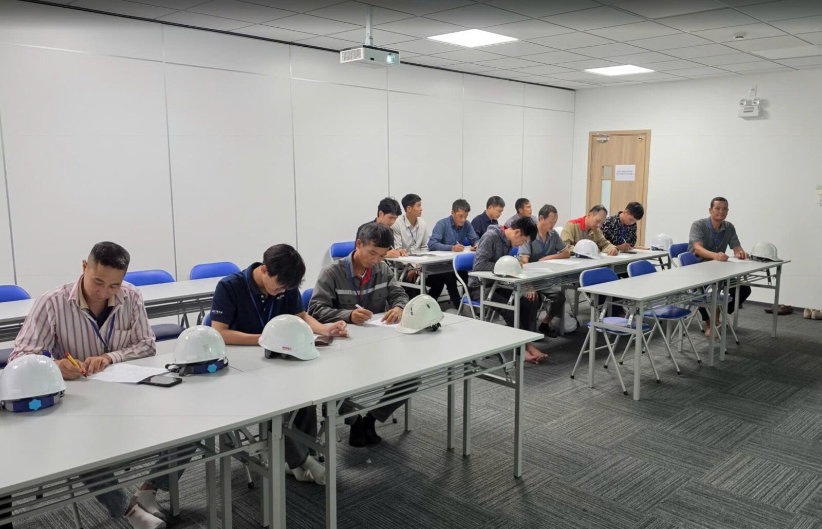 Lớp đào tạo an toàn lao động, học viên ngồi làm bài, mũ bảo hộ đặt trên bàn
