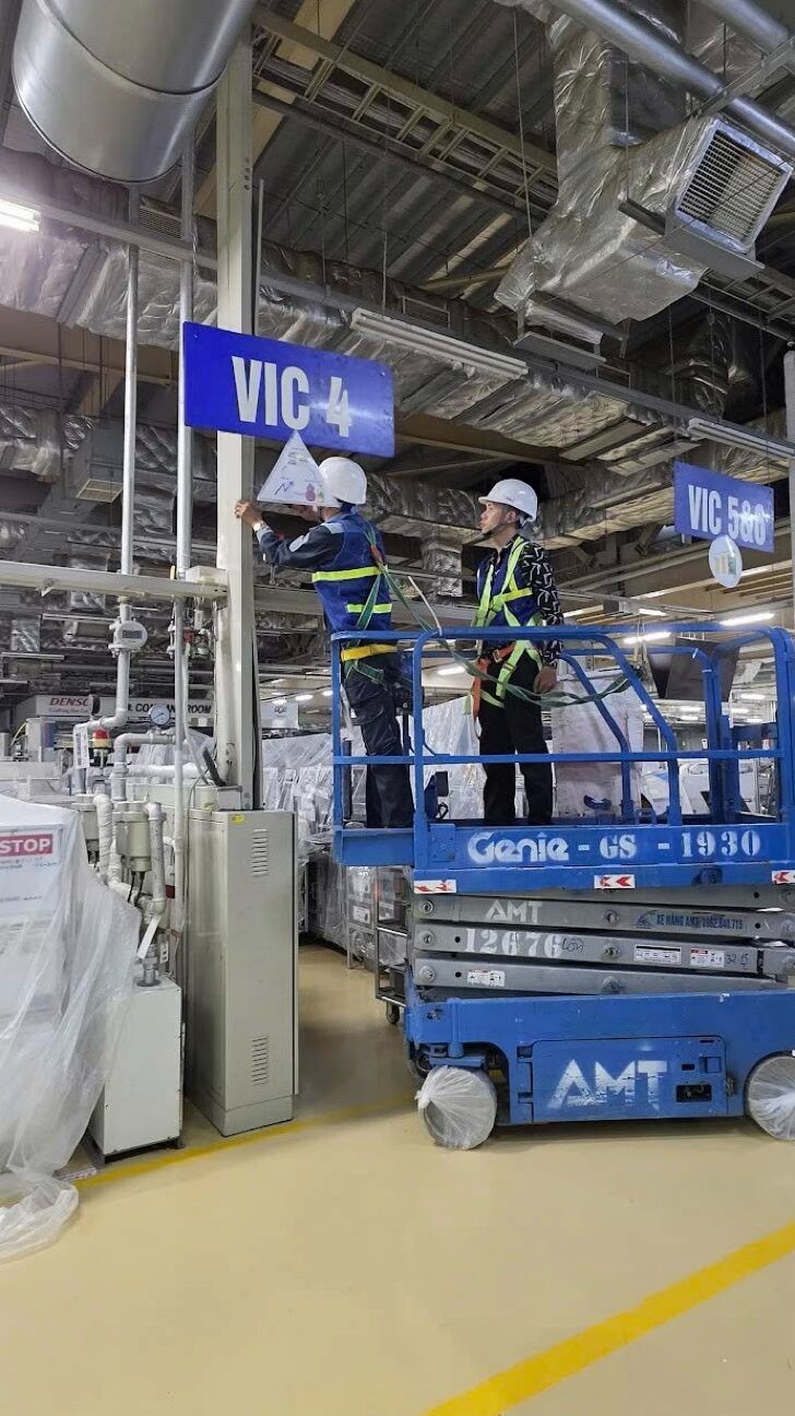 Hai kỹ thuật viên đeo dây an toàn lắp thiết bị trên xe nâng người cạnh biển dây chuyền VIC 4